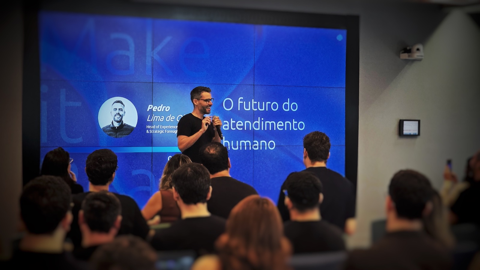 Pedro Lima presenting on stage, with the audience seated in front of him and a screen behind him titled &ldquo;The future of human-centered service.&rdquo;
